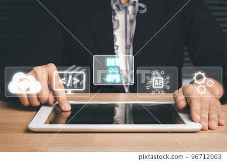 DevOps concept, Man hand touching tablet with DevOps icon on VR screen on desk, Methodology development operations agil programming technology.concept. DevOps concept, Man hand touching tablet with DevOps icon on VR screen on desk, Methodology development operations agil programming technology.concept. 96712003