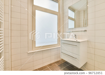 Cupboard with sink and mirror attached to tiled wall near door in modern bathroom 96712851