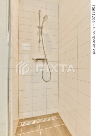 Shower faucet hanging on tiled wall in light washroom in modern flat 96712902
