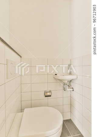 Interior of narrow restroom with sink and wall hung toilet with white walls and tile floor Interior of narrow restroom with sink and wall hung toilet with white walls and tile floor 96712903