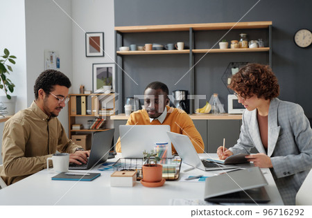 Group of developers sitting at table with computers and working over online project in team during meeting at office 96716292