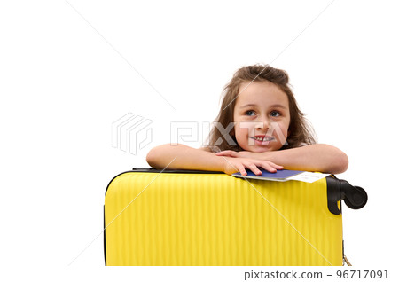 Adorable little passenger girl, with boarding pass and suitcase, traveling abroad for the weekend, smiling toothy smile, dreamily looking away at advertising space. Tourism Tourney Air travel concept 96717091