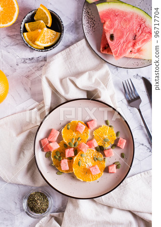 Fresh salad of orange, watermelon and pumpkin seeds on a plate. Organic diet. Top and vertical view Fresh salad of orange, watermelon and pumpkin seeds on a plate. Organic diet. Top and vertical view 96717704