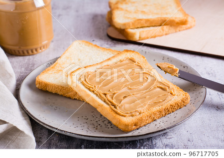 Peanut butter sandwich on toasted bread on a plate and jar of butter on the table Peanut butter sandwich on toasted bread on a plate and jar of butter on the table 96717705