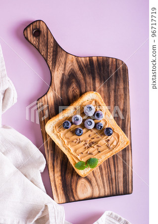 Peanut butter toast with blueberries, flax seeds and mint on a cutting board. Top and vertical view. 96717719