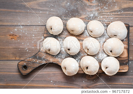 Raw dumplings ready for cooking lie in rows on a wooden cutting board on the table. Top view Raw dumplings ready for cooking lie in rows on a wooden cutting board on the table. Top view 96717872