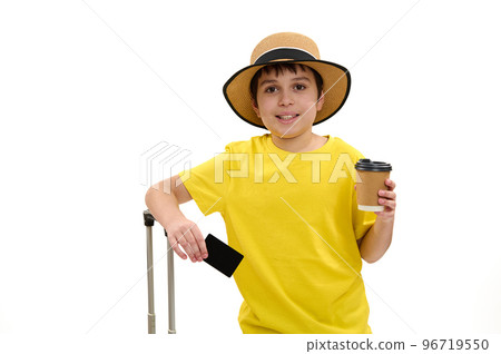 Adorable teenage boy - young tourist in bright yellow t-shirt and straw hat, standing over white background with blank plastic credit card, takeaway drink in paper cup and suitcase. Travel. Journey Adorable teenage boy - young tourist in bright yellow t-shirt and straw hat, standing over white background with blank plastic credit card, takeaway drink in paper cup and suitcase. Travel. Journey 96719550