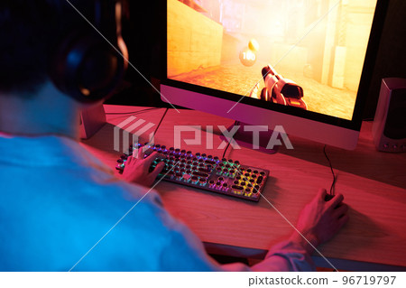 Teenage boy playing first person shooter videogame, view over the shoulder 96719797