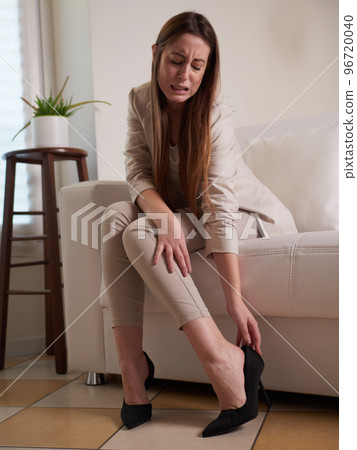 Woman taking off  high heels shoes after work and massages painful feet at home on white couch. 96720040