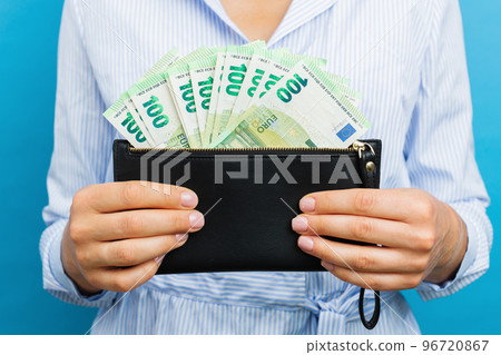 Female hands holding black wallet with euro banknotes on a blue background. Female hands holding black wallet with euro banknotes on a blue background. 96720867