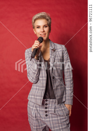 Beautiful blonde host singer blogger woman in suit holding microphone on red background 96721111