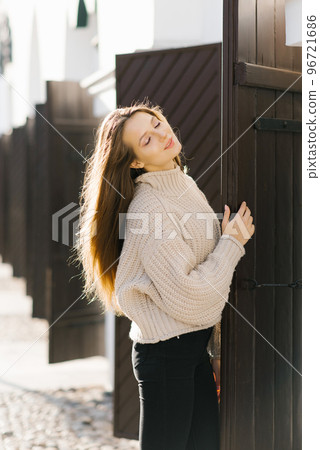 A rather fashionable young woman in a knitted sweater and black jeans is enjoying a walk along the city street. Attractive girl in fashionable clothes in the city. A rather fashionable young woman in a knitted sweater and black jeans is enjoying a walk along the city street. Attractive girl in fashionable clothes in the city. 96721686