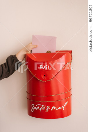 A child puts a letter to Santa Claus in a red Christmas mailbox A child puts a letter to Santa Claus in a red Christmas mailbox 96721805