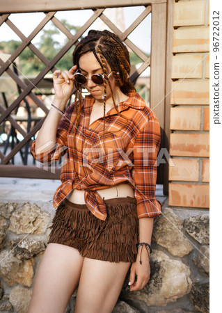 a girl with a dreadlocked hairstyle poses in summer outdoor, bright sunlight, dressed in a plaid shirt and shorts a girl with a dreadlocked hairstyle poses in summer outdoor, bright sunlight, dressed in a plaid shirt and shorts 96722012