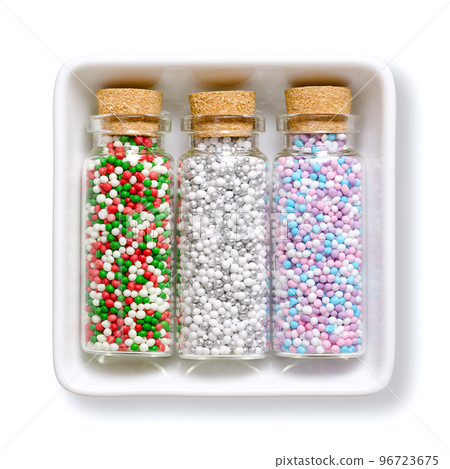 Nonpareils, in small glass bottles, in a white bowl. Winter and christmas colored mixes of edible confectionery of tiny sugar balls. Hundreds and Thousands, used as a sweet decoration and as topping. 96723675