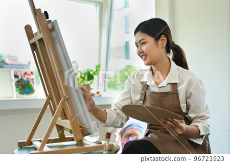 Attractive female artist painting with watercolor on canvas in art workshop. Art, creative hobby and leisure activity concept Attractive female artist painting with watercolor on canvas in art workshop. Art, creative hobby and leisure activity concept 96723923