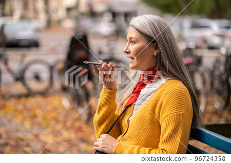 Good-looking woman sitting on the bench and talking on the phone 96724358
