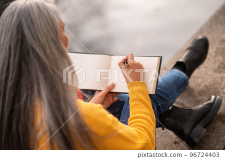 Inspired woman with an albom in hands on the river bank Inspired woman with an albom in hands on the river bank 96724403