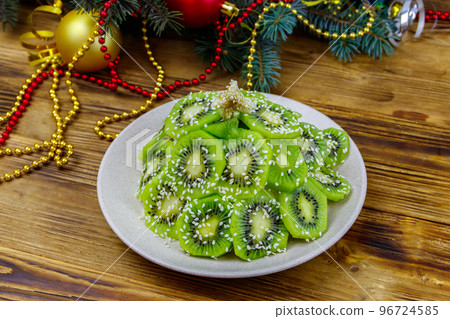 Christmas tree shaped fruit salad and Christmas decorations on wooden table. Creative idea for Christmas and New Year festive desserts. Funny food idea for kids Christmas tree shaped fruit salad and Christmas decorations on wooden table. Creative idea for Christmas and New Year festive desserts. Funny food idea for kids 96724585