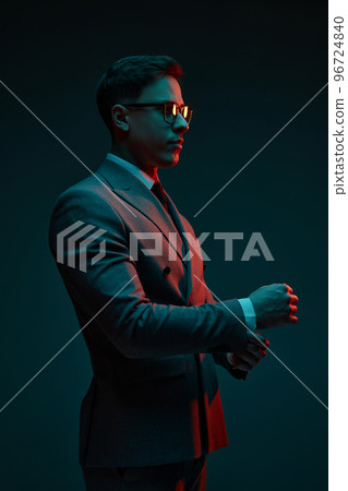 Fashionable serious young businessman in classic style suit adjusting his jacket sleeve isolated over dark background in neon light. Fashion look of businessman. Office style 96724840