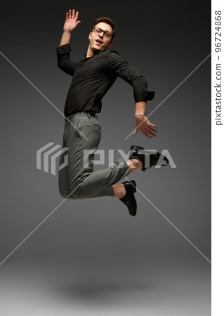 High jumps. Happy young man, student, business in black classic style shirt and grey trousers running, jumping isolated over grey background. Modern office style 96724868