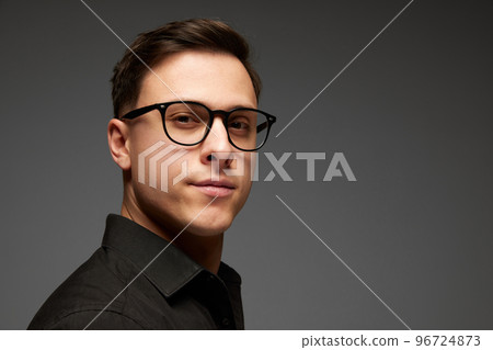 Closeup. Young businessman in black business classic style shirt looks at camera with confident look isolated over grey background. Fashion look of businessman. 96724873