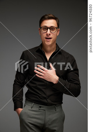 Surprised young man in black business classic style shirt and grey trousers looking at camera with surprise isolated over grey background. Modern office style 96724880