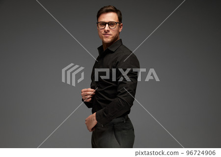 Smiling confident young man in black business classic style shirt and grey trousers posing isolated over grey background. Fashion look of businessman. Office style 96724906