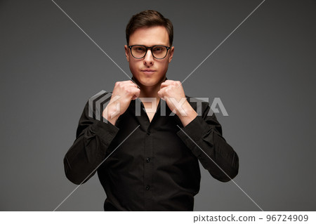 Confident young man in black business classic style shirt and grey trousers posing isolated over grey background. Fashion look of businessman. Office style Confident young man in black business classic style shirt and grey trousers posing isolated over grey background. Fashion look of businessman. Office style 96724909