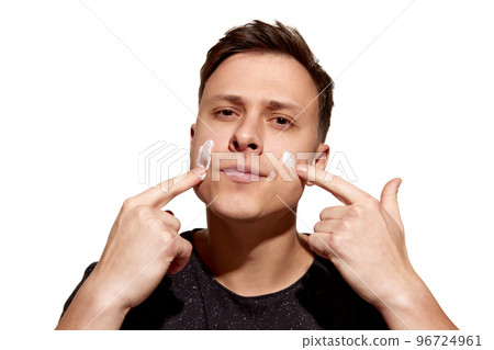 Facial skin care for man. Young attractive man with perfect well-kept skin using face cream isolated over white background. Cosmetics, health care, skin care, beauty Facial skin care for man. Young attractive man with perfect well-kept skin using face cream isolated over white background. Cosmetics, health care, skin care, beauty 96724961