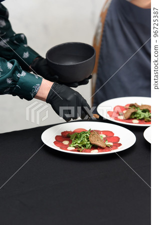 white dish with carpaccio of beef. the chef is preparing to serve a meal in a restaurant 96725387
