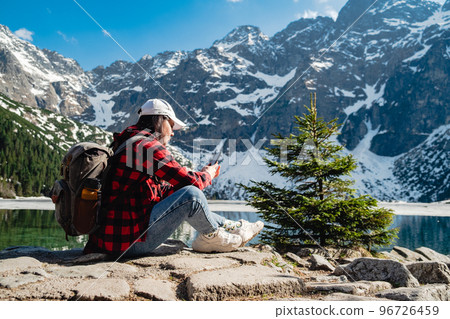 A woman is sitting on the shore of a lake. Morskie Oko, Tatras mountains. A woman is sitting on the shore of a lake. Morskie Oko, Tatras mountains. 96726459