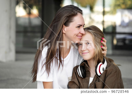 Mother hugs with daughter schoolgirl outdoors. Cheerful teen and female in good mood. Love and family concept 96728546