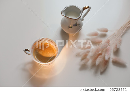 cup with coffee and milk jug on a white wooden background, closeup. Energy breakfast, morning routine concept 96728551
