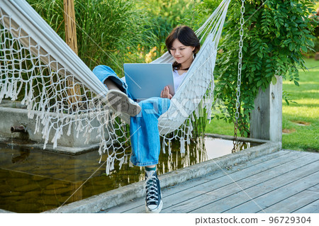 Teenage girl relaxing in hammock using laptop for leisure study Teenage girl relaxing in hammock using laptop for leisure study 96729304