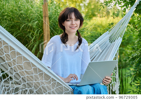 Teenage girl relaxing in hammock using laptop for leisure study Teenage girl relaxing in hammock using laptop for leisure study 96729305