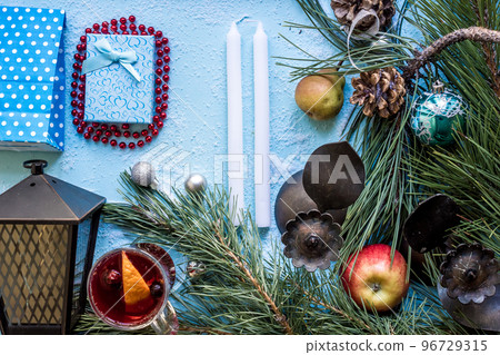 Hot mulled wine with orange, anise, cardamon and cinnamon on blue background. Christmas tree branches, gifts and cones. 96729315