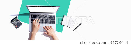 Person using a laptop computer with a notebook 96729444