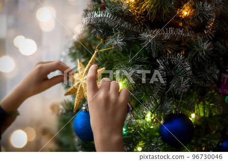 The hands of a child decorating an artificial Christmas tree with a gold star. The atmosphere of preparation for the holiday. The dark key. Zero waste. The hands of a child decorating an artificial Christmas tree with a gold star. The atmosphere of preparation for the holiday. The dark key. Zero waste. 96730046