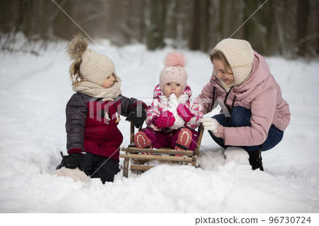 Mom and children on a vintage wooden sled against the backdrop of a winter forest. Woman with children on a winter walk. 96730724