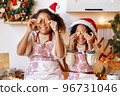 Happy ethnic children on Christmas eve,   girl and boy covers eyes with cookies gingerbreads that they baked and laughs  in cozy kitchen 96731046