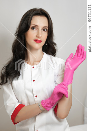A beautiful and young cosmetologist puts on latex disposable gloves. 96731131