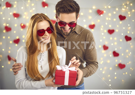 Loving couple unpacks a gift for Valentine's Day standing on a background of garlands and hearts. 96731327