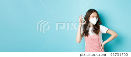 Covid, health and pandemic concept. Very good. Young supportive woman wearing medical respirator and showing okay sign in approval, praise wearing face masks in public, blue background Covid, health and pandemic concept. Very good. Young supportive woman wearing medical respirator and showing okay sign in approval, praise wearing face masks in public, blue background 96731700