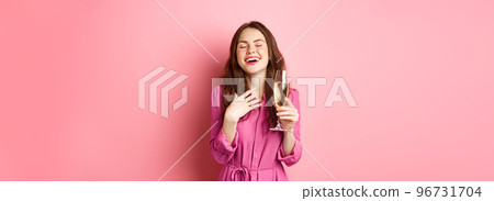 Celebration and holidays concept. Stylish coquettish woman in trendy dress, holding glass of champagne at party, smiling pleased, standing over pink background 96731704