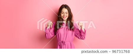 Attractive female model in spring outfit, pointing and looking down, showing copyspace aside, standing against pink background Attractive female model in spring outfit, pointing and looking down, showing copyspace aside, standing against pink background 96731768
