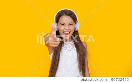 teen girl listen music in headphones on yellow background. point finger teen girl listen music in headphones on yellow background. point finger 96732433
