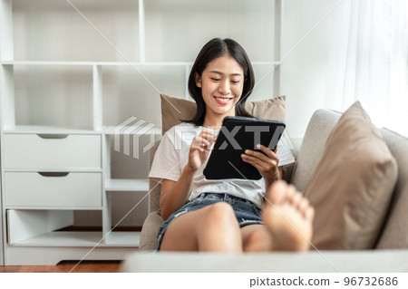 Half-Japanese woman sitting on the sofa using tablet while on vacation, Rest at home, Living room, Relax time, Touch screen tablet, Go on internet, Favorite corner, Personal space 96732686