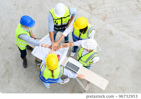 Top view of contractors, engineers and formats team in safety vests with helmets working with laptops, standing on under-construction building site. Home building project. Engineer foreman discusses Top view of contractors, engineers and formats team in safety vests with helmets working with laptops, standing on under-construction building site. Home building project. Engineer foreman discusses 96732953