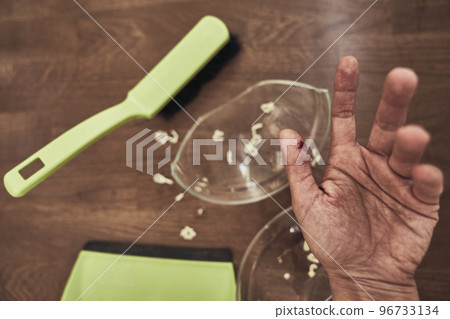 Close-up of a cut female finger on the background of a split cup and a brush with a dustpan for cleaning. A wound with blood received when cleaning broken dishes. High quality photo 96733134